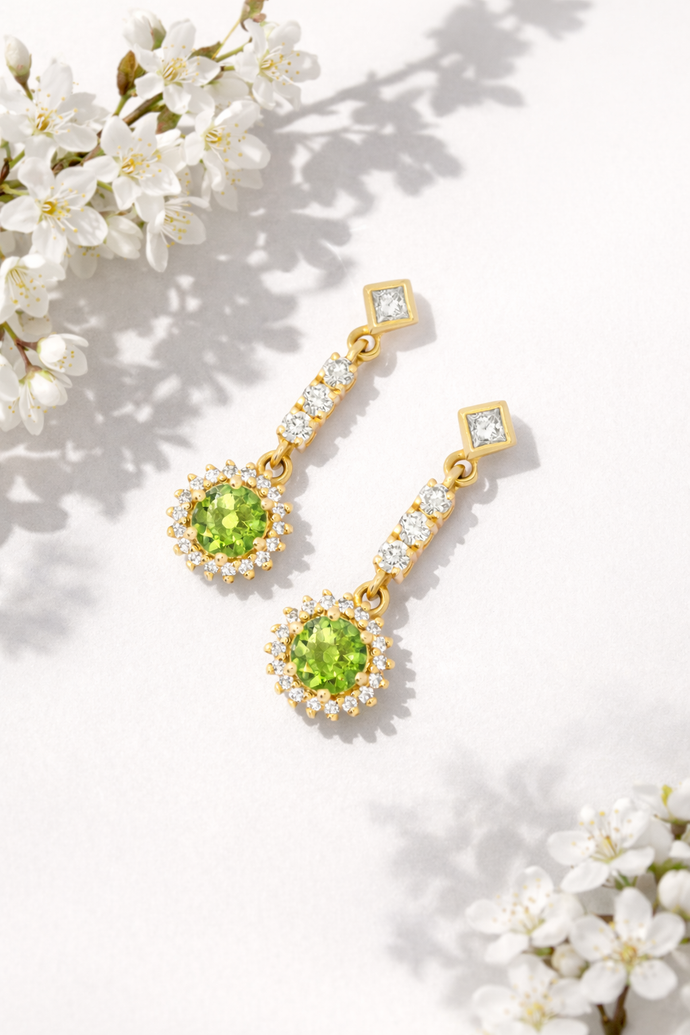 Handcrafted Emessa Tsavorite and natural diamond drop earrings with green centre stones, styled with white flowers on a soft neutral background.