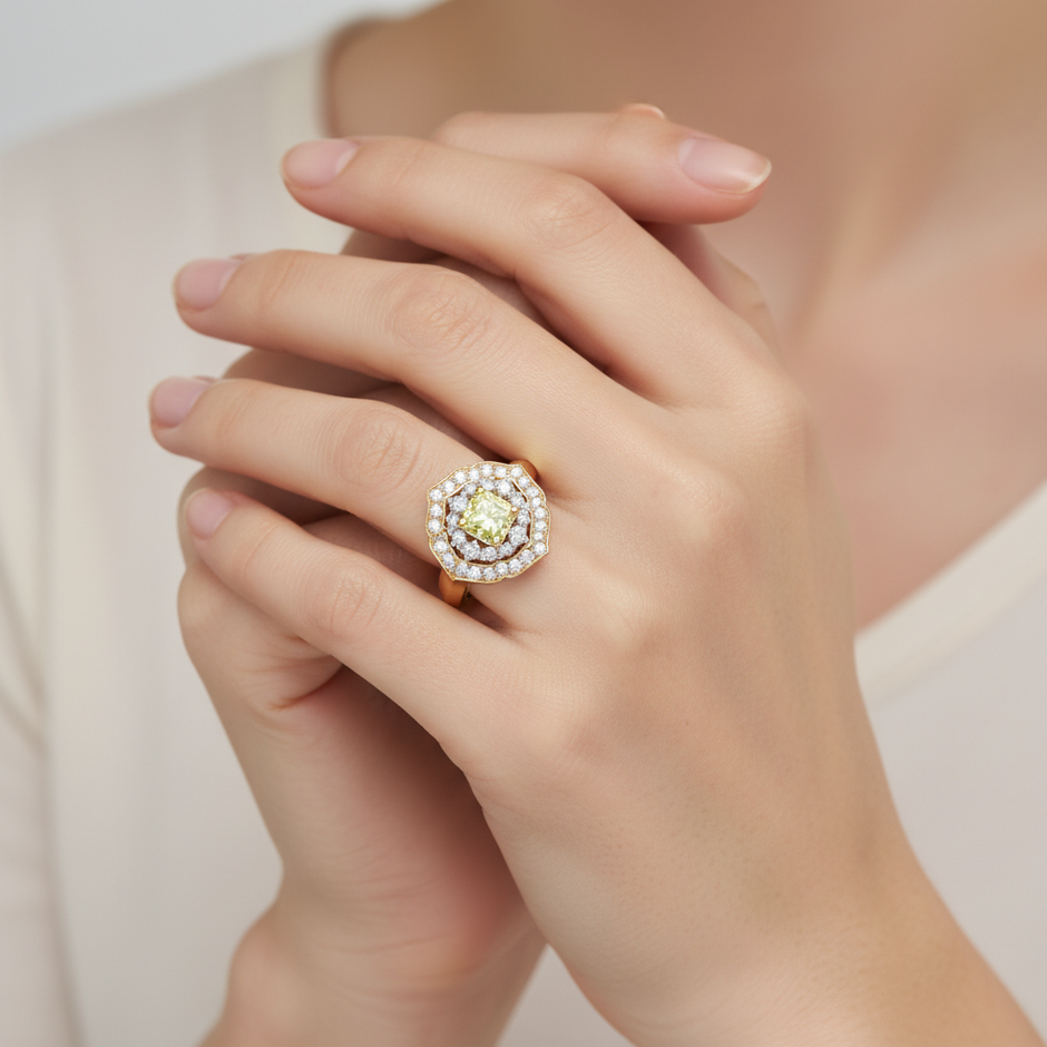A close-up of a hand wearing a luxurious cocktail ring featuring a vibrant, cushion-cut Canary yellow diamond centre stone, surrounded by a double halo of brilliant white diamonds set in yellow gold.